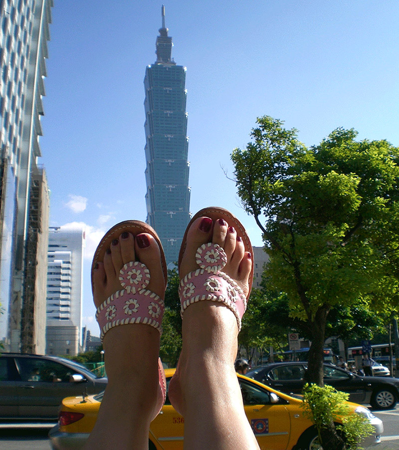 Vanessa Blaylock's feet in sandals, hanging out a car window in Taipei with the Taipei 101 tower in the background