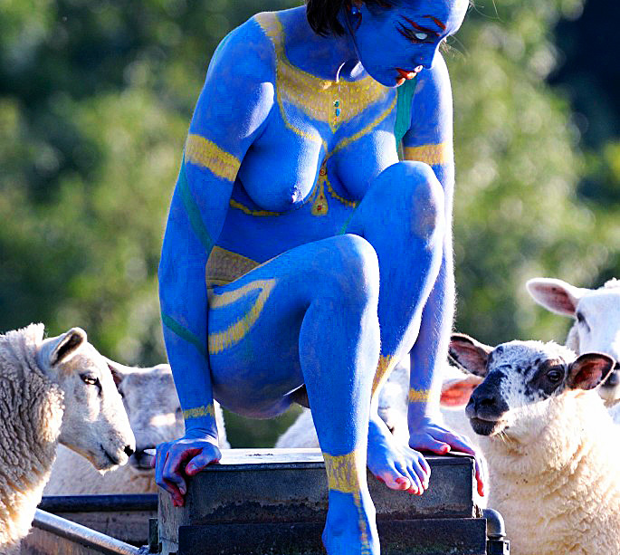 woman painted blue as Kali, surrounded by sheep at trough