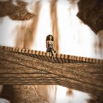 The tiny figure of Vaneeesa Blaylock sits on a wooden bridge with an enormous waterfall at her back.