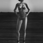 Black and white photograph of Vaneeesa Blaylock recreating Helmut Newton's photograph "Big Nude I" which is a full length nude portrait, wearing heels and facing forward with arms akimbo