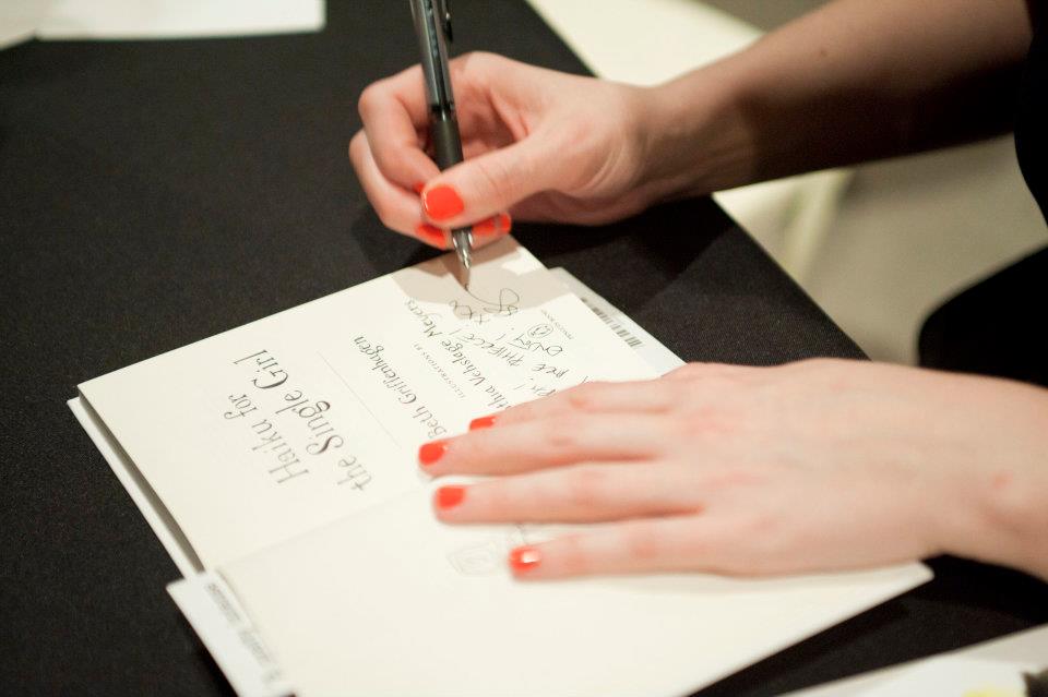Photograph of Beth Griffenhagen autographing her book 'Haiku for the Single Girl' - image shows a book on a table with a pair of hands (Griffenhagen's) signing on the title page