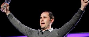 Photo of Twitter co-founder Evan Williams in a grey sweater with arms outstretched as he addresses an audience.