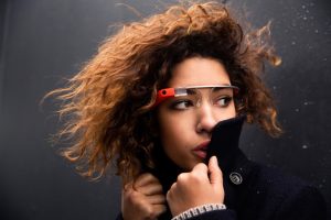 Google Fangirl Vanessa Blaylock, her teased hair blowing in the wind, wears a red pair of google glass and turns across the frame into the collar of a trench coat